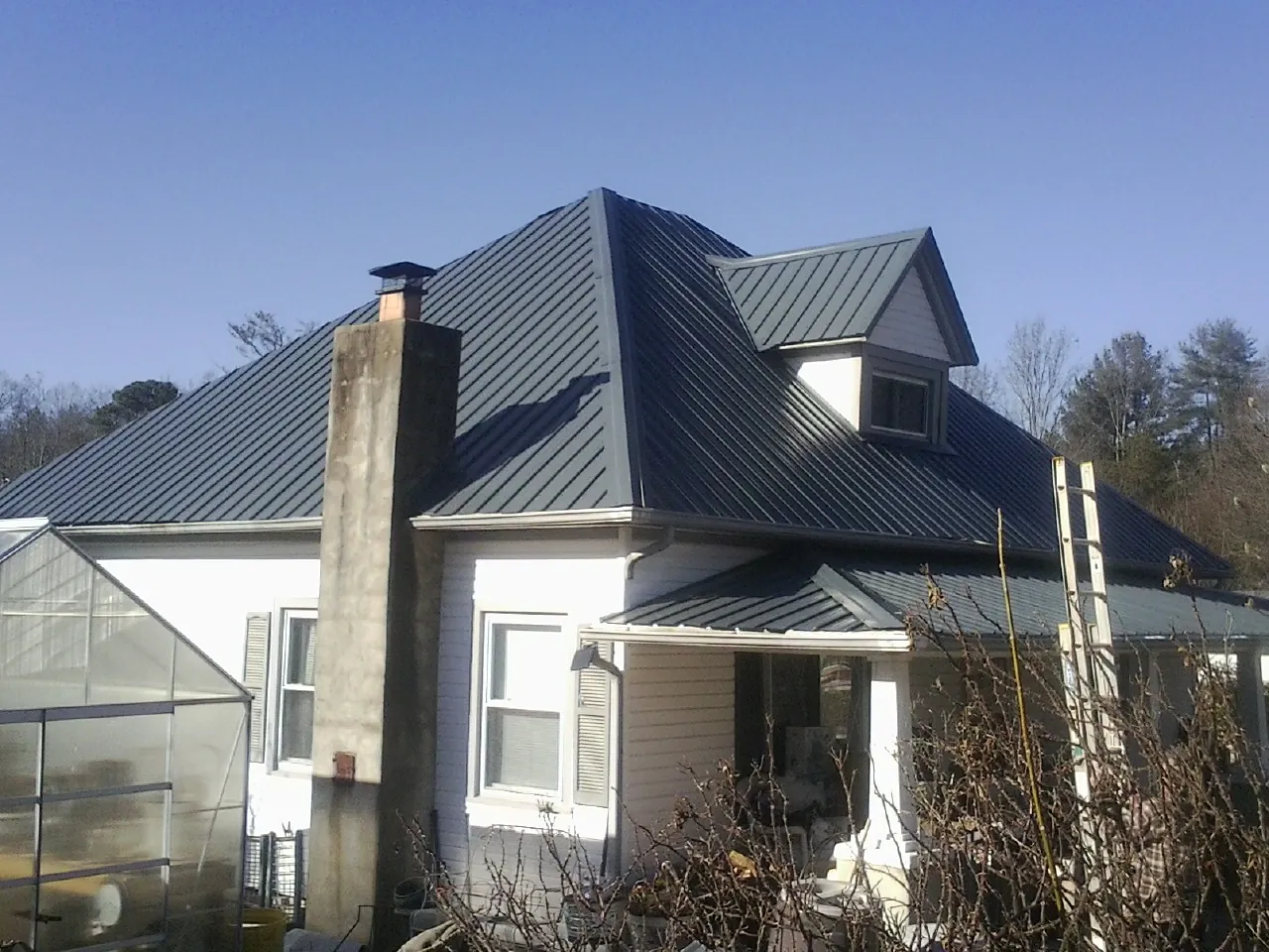 Dark blue standing seam metal roof on a white farmhouse with dormer — Slate & Tile Roof Repair by Roofing Brothers in Broadview Heights