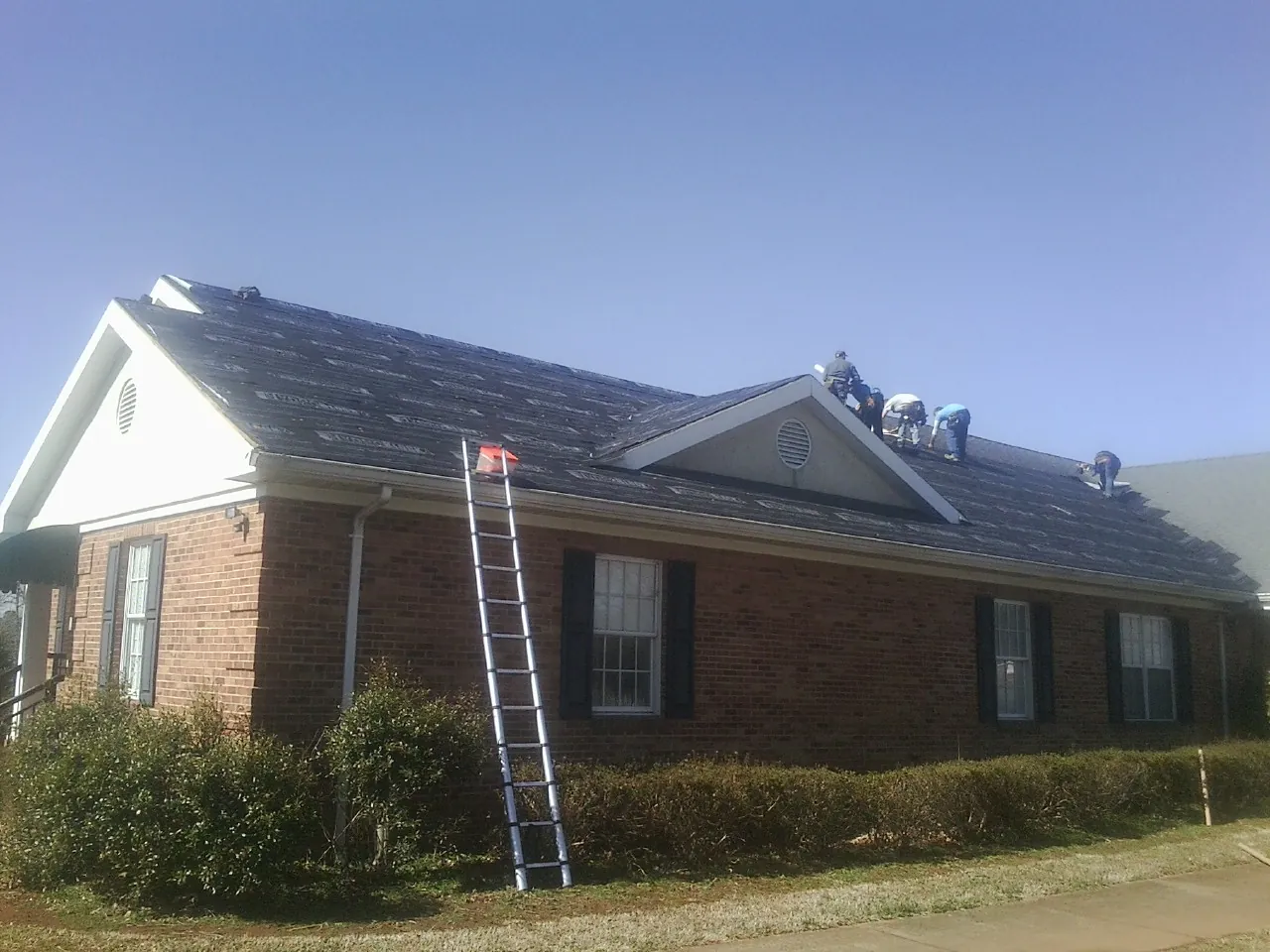 Crew tearing shingles off a brick ranch roof with a ladder set — Metal Roof Repair work by our crew in Broadview Heights
