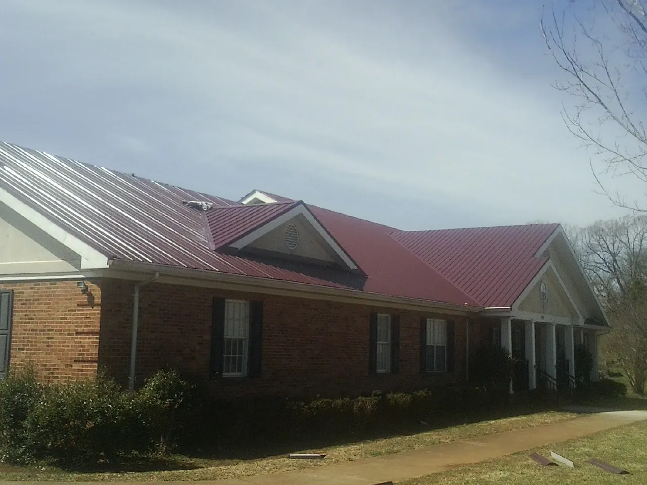 Red metal roof with gabled entries on a long brick building, from a Hail Damage Roof Repair job in Broadview Heights
