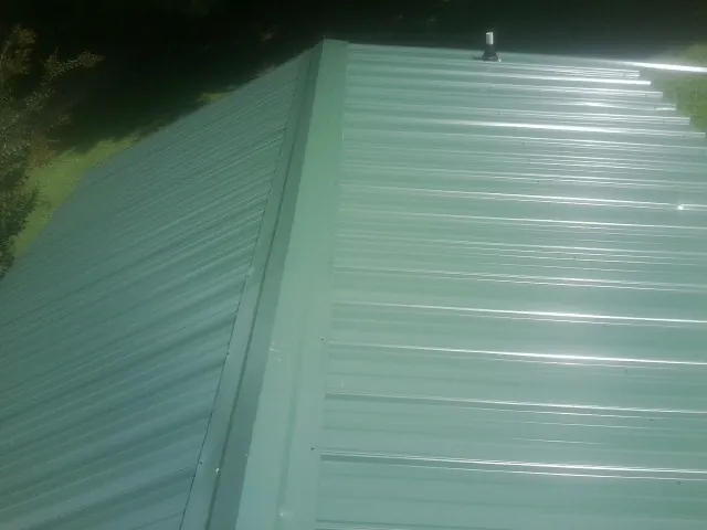 New green metal panels meeting at the ridge of a roof — Flat Roof Repair work by our crew in Broadview Heights