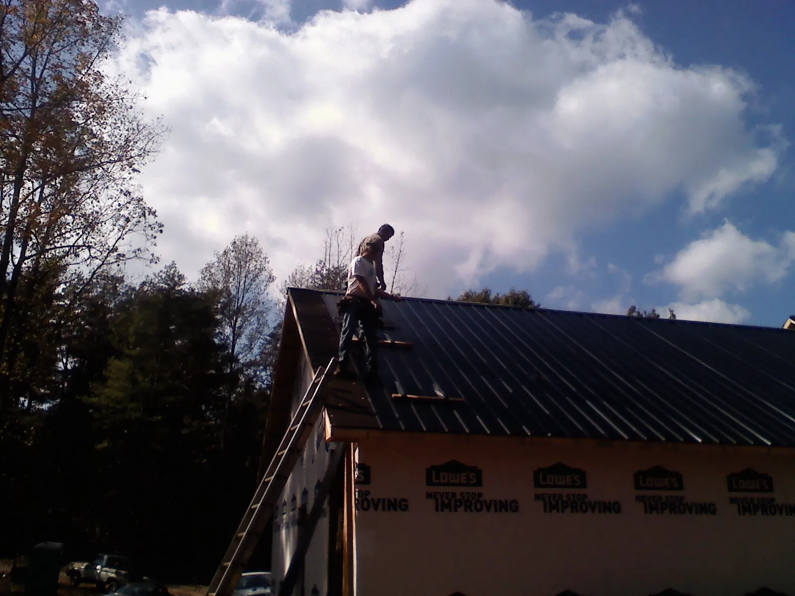 Roofer fastening dark metal panels high against a cloudy sky, from a Roof Inspection job in Broadview Heights