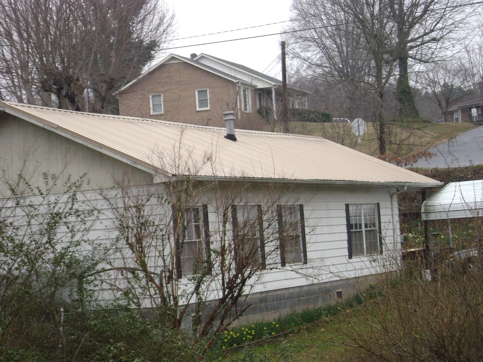 Tan metal roof on a white sided house set into a hillside — Commercial Roofing by Roofing Brothers in Broadview Heights